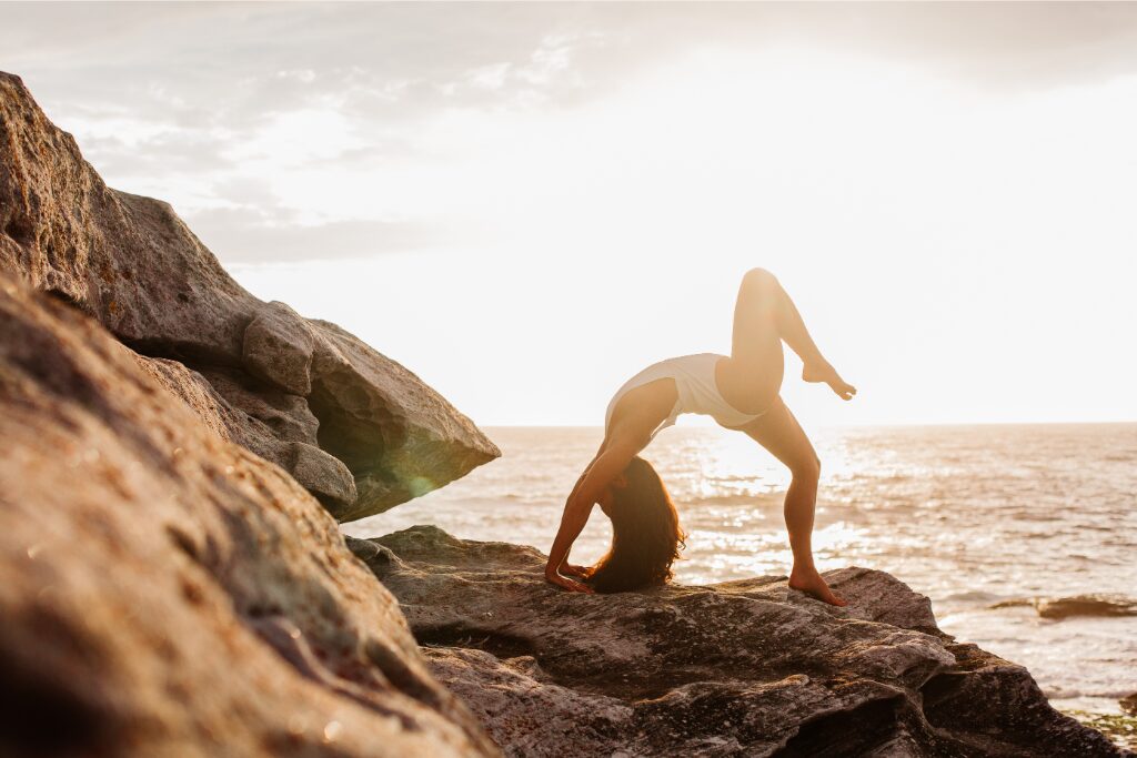 Une femme fais une position de yoga inversée sur les mains sur des rochers. 